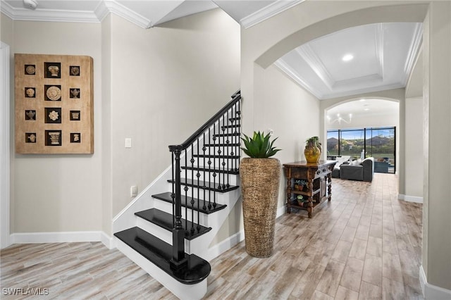 stairs with crown molding, arched walkways, baseboards, and wood finished floors