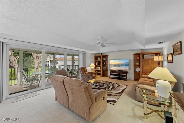 living room featuring ceiling fan, a tray ceiling, light carpet, and a textured ceiling