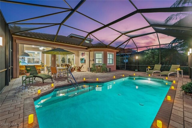 pool at dusk with glass enclosure and a patio area