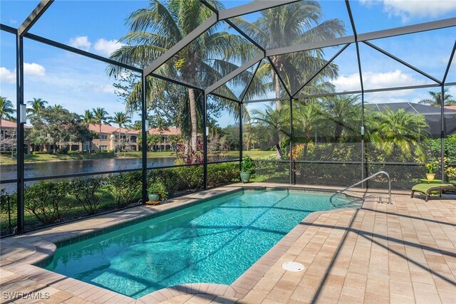 view of pool with glass enclosure, a patio area, and a water view