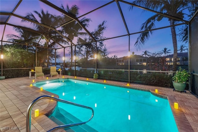 pool at dusk featuring glass enclosure and a patio area