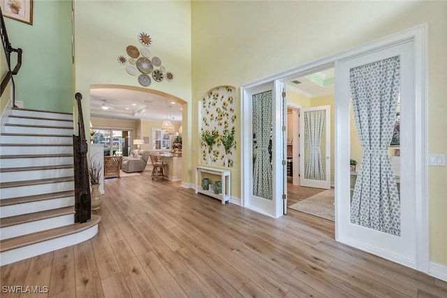 foyer entrance with a towering ceiling, ornamental molding, a raised ceiling, and light wood-type flooring