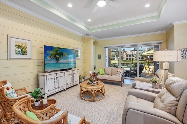 living room featuring ceiling fan, a raised ceiling, crown molding, and wooden walls