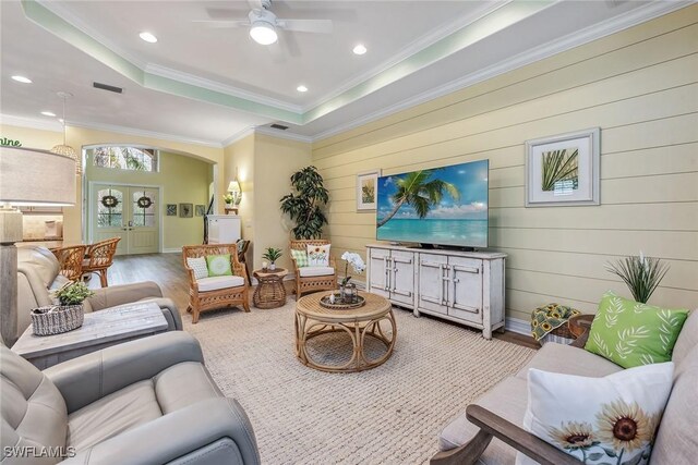 living room featuring ceiling fan, a tray ceiling, light hardwood / wood-style flooring, and crown molding