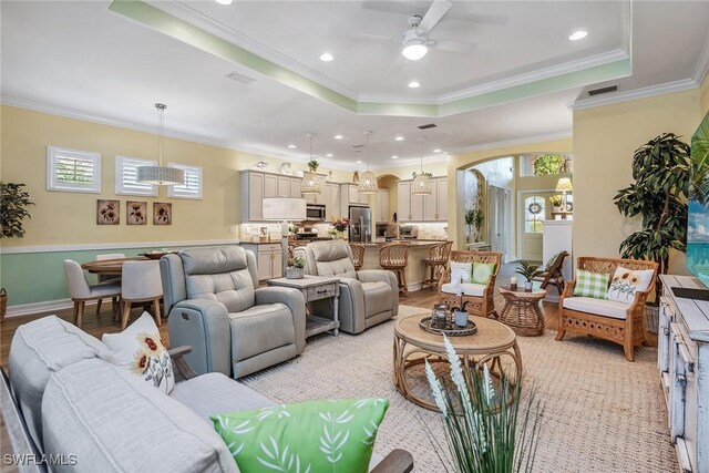 living room featuring crown molding, light wood-type flooring, ceiling fan, and a tray ceiling