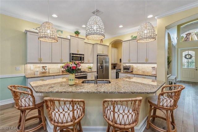 kitchen featuring stainless steel appliances, a kitchen breakfast bar, hanging light fixtures, light stone counters, and a center island with sink