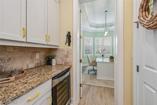 bar featuring ornamental molding, a tray ceiling, beverage cooler, light stone countertops, and white cabinets