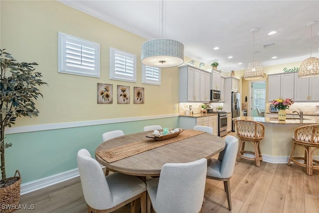 dining room with light wood-type flooring, a healthy amount of sunlight, and crown molding