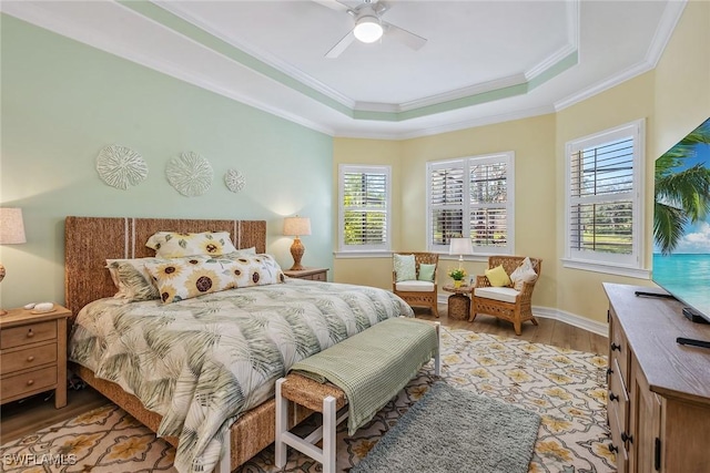 bedroom featuring ornamental molding, light hardwood / wood-style flooring, ceiling fan, and a raised ceiling