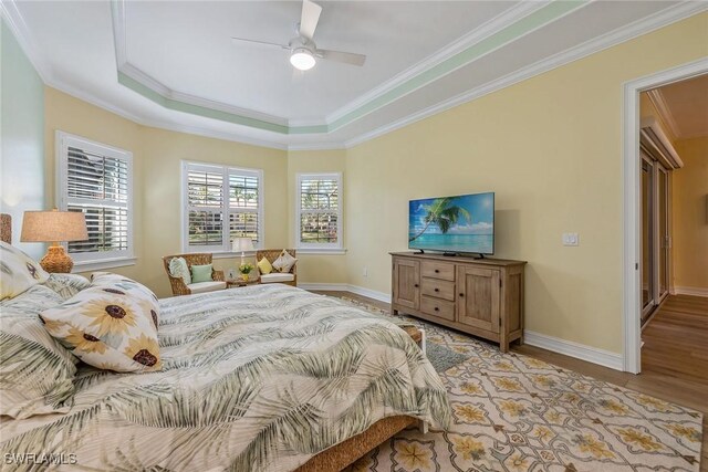 bedroom with light hardwood / wood-style flooring, a tray ceiling, ceiling fan, and ornamental molding