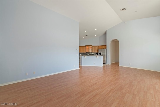 unfurnished living room featuring high vaulted ceiling and light hardwood / wood-style floors