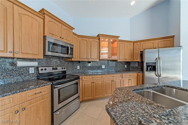 kitchen featuring sink, dark stone countertops, decorative backsplash, light tile patterned floors, and stainless steel appliances