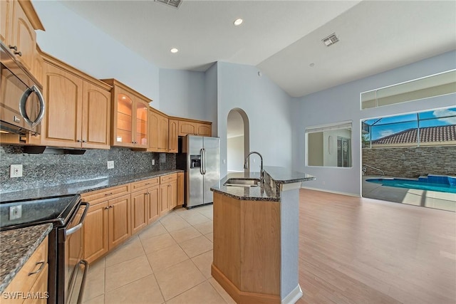 kitchen featuring appliances with stainless steel finishes, high vaulted ceiling, sink, dark stone countertops, and backsplash