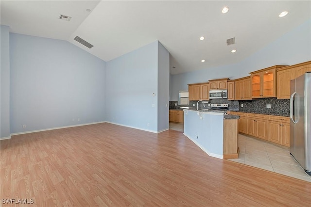 kitchen featuring appliances with stainless steel finishes, an island with sink, sink, dark stone countertops, and light wood-type flooring