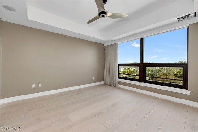 empty room featuring a tray ceiling, light wood-style flooring, baseboards, and a ceiling fan