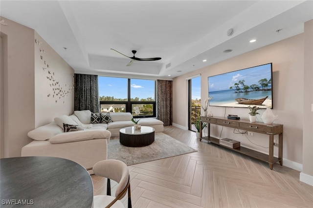 living room featuring light parquet floors, a raised ceiling, and ceiling fan