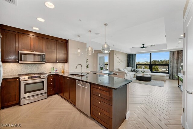 kitchen with stainless steel appliances, sink, dark stone counters, pendant lighting, and light parquet flooring