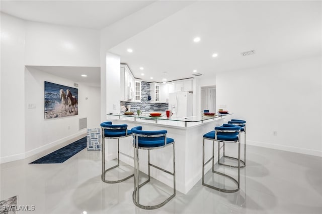 kitchen featuring white refrigerator with ice dispenser, visible vents, backsplash, white cabinetry, and a kitchen bar