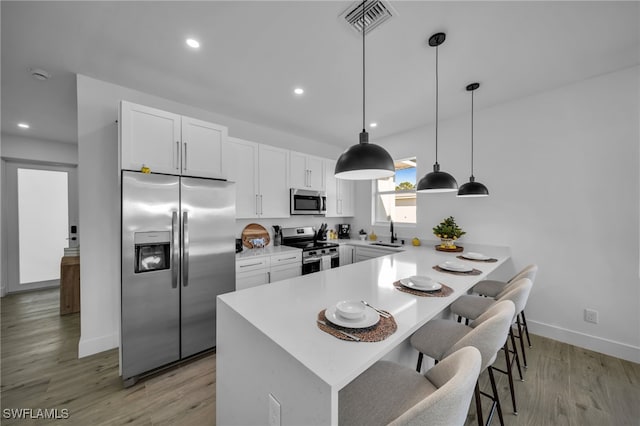 kitchen featuring a kitchen breakfast bar, pendant lighting, stainless steel appliances, light hardwood / wood-style floors, and white cabinets