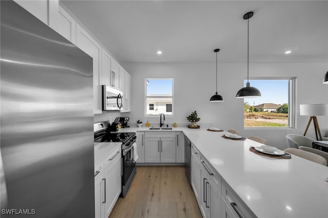 kitchen with sink, hanging light fixtures, plenty of natural light, appliances with stainless steel finishes, and white cabinets