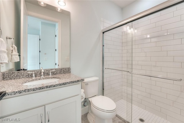 bathroom featuring vanity, a shower with door, and toilet