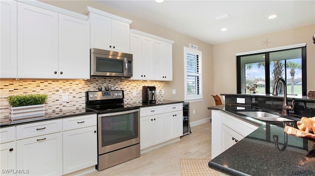 kitchen featuring appliances with stainless steel finishes, sink, white cabinets, tasteful backsplash, and light wood-type flooring