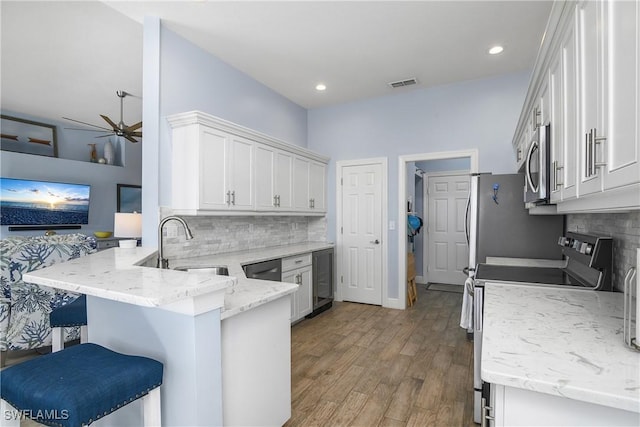 kitchen with appliances with stainless steel finishes, white cabinetry, a kitchen breakfast bar, kitchen peninsula, and light stone countertops