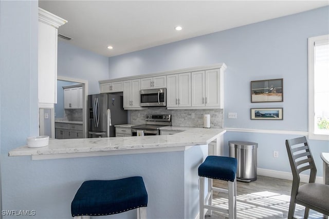 kitchen featuring white cabinetry, stainless steel appliances, kitchen peninsula, and a breakfast bar