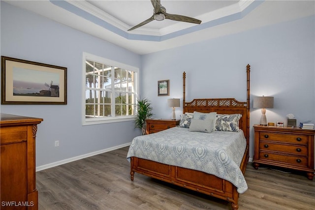 bedroom featuring crown molding, dark wood-type flooring, a raised ceiling, and ceiling fan