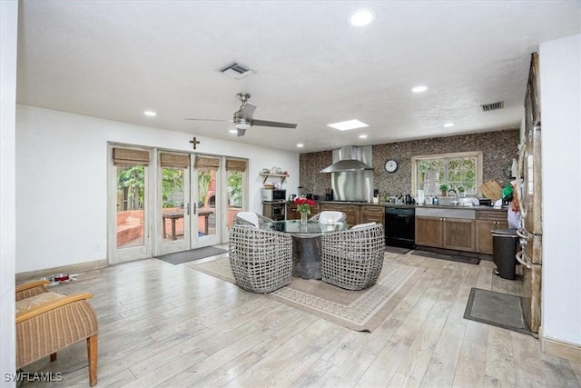 kitchen with light hardwood / wood-style flooring, black dishwasher, wall chimney range hood, and french doors