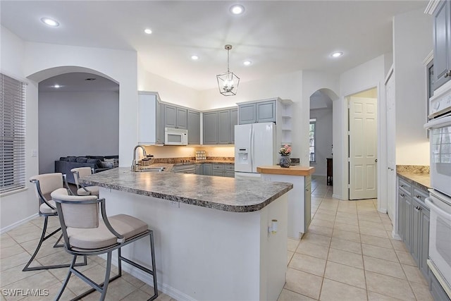 kitchen with pendant lighting, white appliances, sink, kitchen peninsula, and light tile patterned flooring