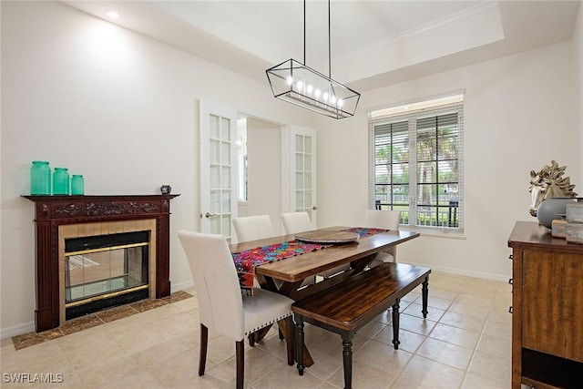 dining room featuring light tile patterned floors, french doors, a raised ceiling, ornamental molding, and a tiled fireplace