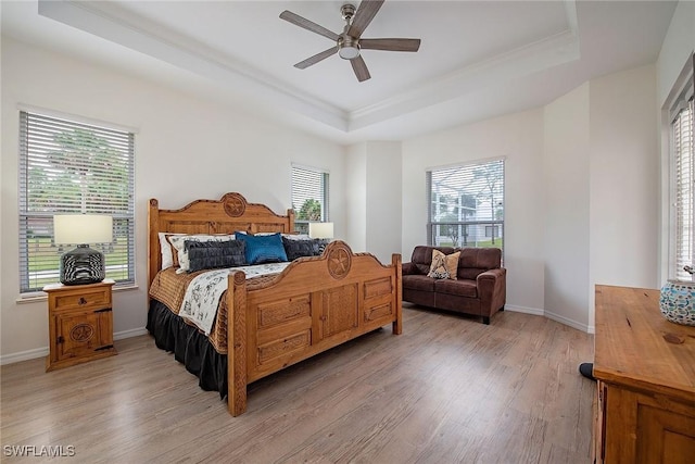 bedroom featuring multiple windows, light hardwood / wood-style flooring, ceiling fan, and a raised ceiling