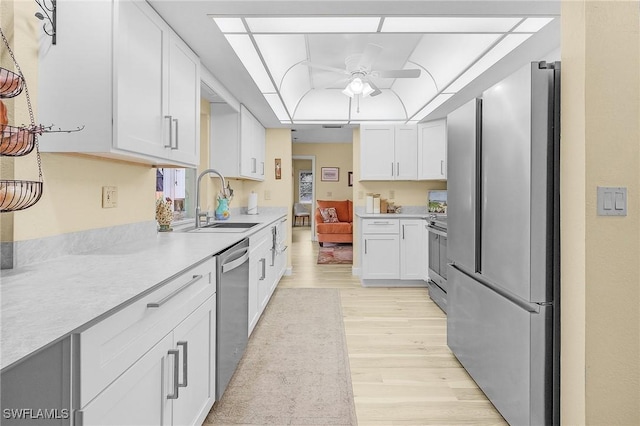 kitchen with ceiling fan, sink, white cabinets, light wood-type flooring, and stainless steel appliances