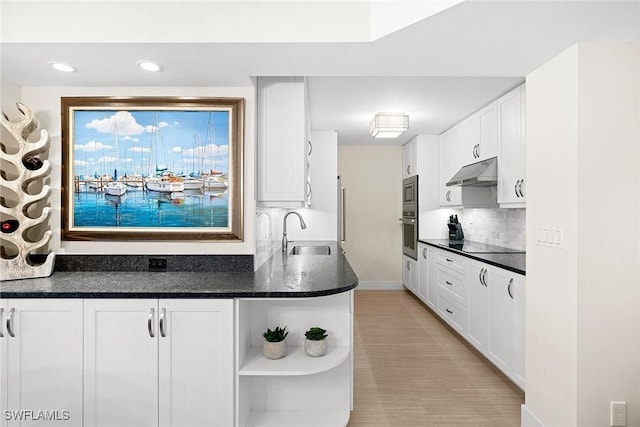 kitchen featuring stainless steel microwave, sink, backsplash, white cabinets, and dark stone counters