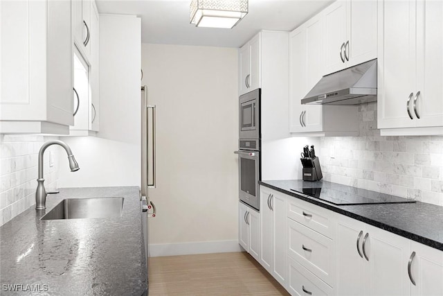 kitchen with appliances with stainless steel finishes, dark stone counters, sink, white cabinets, and backsplash