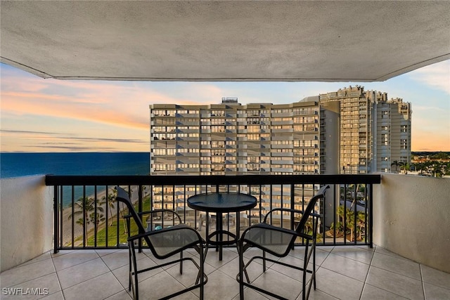 balcony at dusk featuring a water view