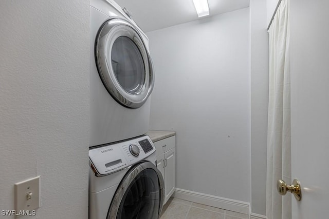 clothes washing area featuring stacked washer / dryer, cabinets, and light tile patterned floors