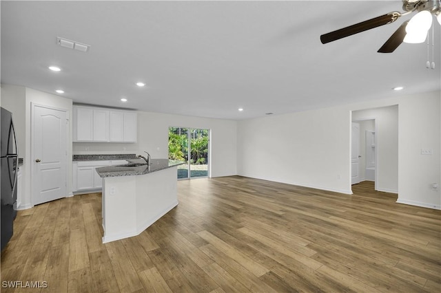 kitchen with white cabinetry, light wood-type flooring, dark stone countertops, sink, and an island with sink