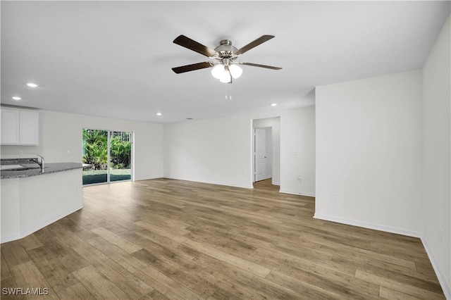 unfurnished living room with sink, light hardwood / wood-style floors, and ceiling fan