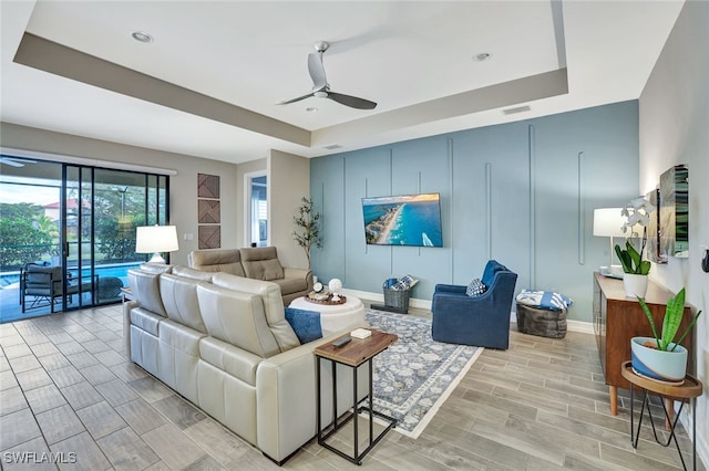 living room featuring ceiling fan and a raised ceiling