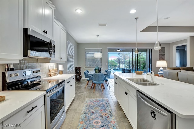 kitchen featuring white cabinetry, appliances with stainless steel finishes, pendant lighting, and an island with sink