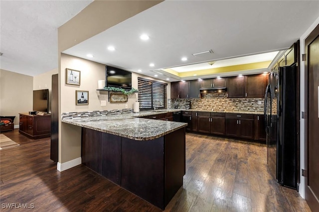 kitchen with black refrigerator, dark wood-type flooring, light stone countertops, and kitchen peninsula