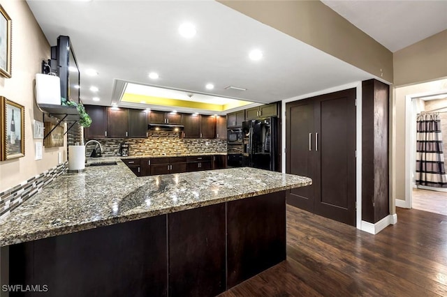 kitchen with black appliances, sink, kitchen peninsula, light stone countertops, and dark wood-type flooring