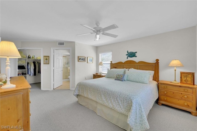 bedroom featuring connected bathroom, a spacious closet, light colored carpet, ceiling fan, and a closet