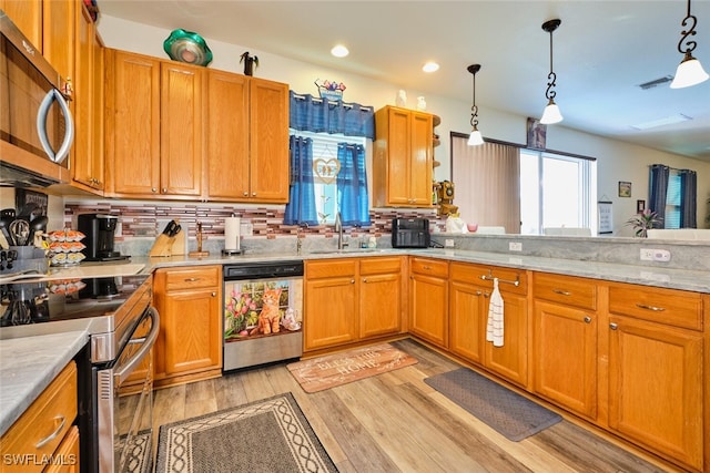 kitchen with hanging light fixtures, appliances with stainless steel finishes, sink, and light wood-type flooring