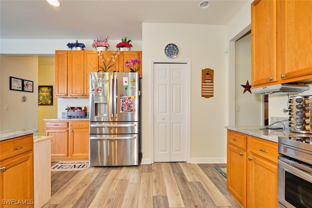 kitchen featuring light stone countertops, stainless steel fridge, light hardwood / wood-style floors, and range