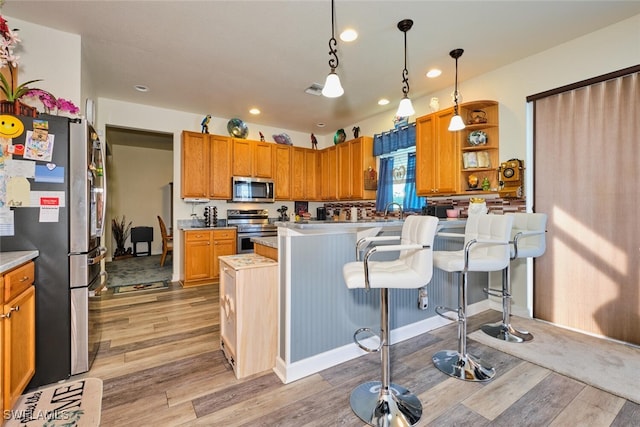 kitchen featuring pendant lighting, a breakfast bar area, a center island, stainless steel appliances, and light wood-type flooring