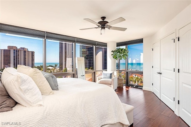 bedroom with a water view, ceiling fan, floor to ceiling windows, and dark hardwood / wood-style floors