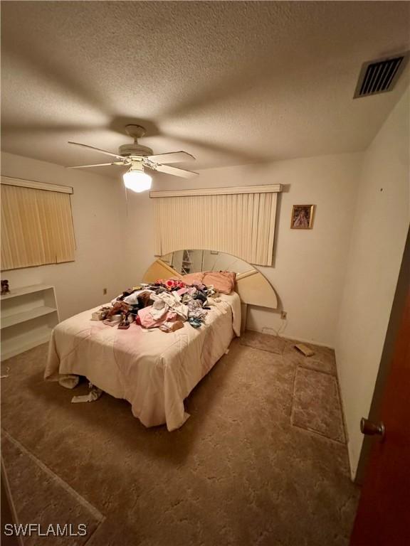 carpeted bedroom with ceiling fan and a textured ceiling